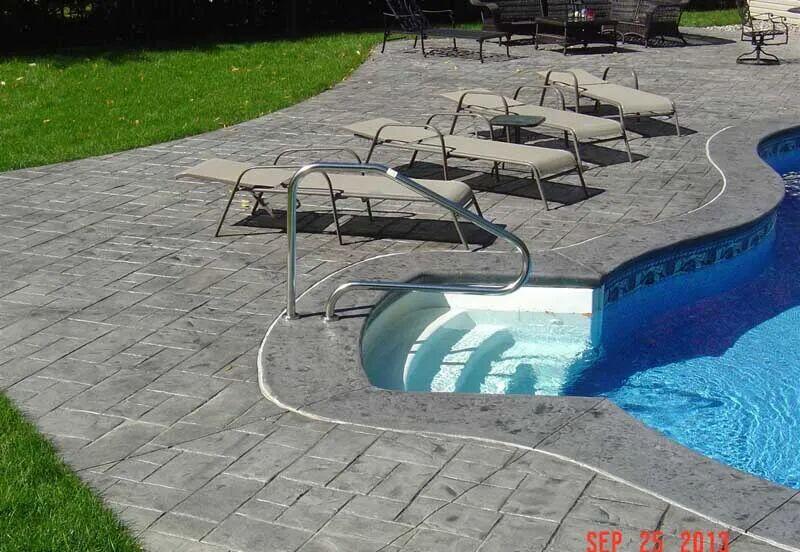 Gray ashlar stamped pool deck with loungers and pool steps
