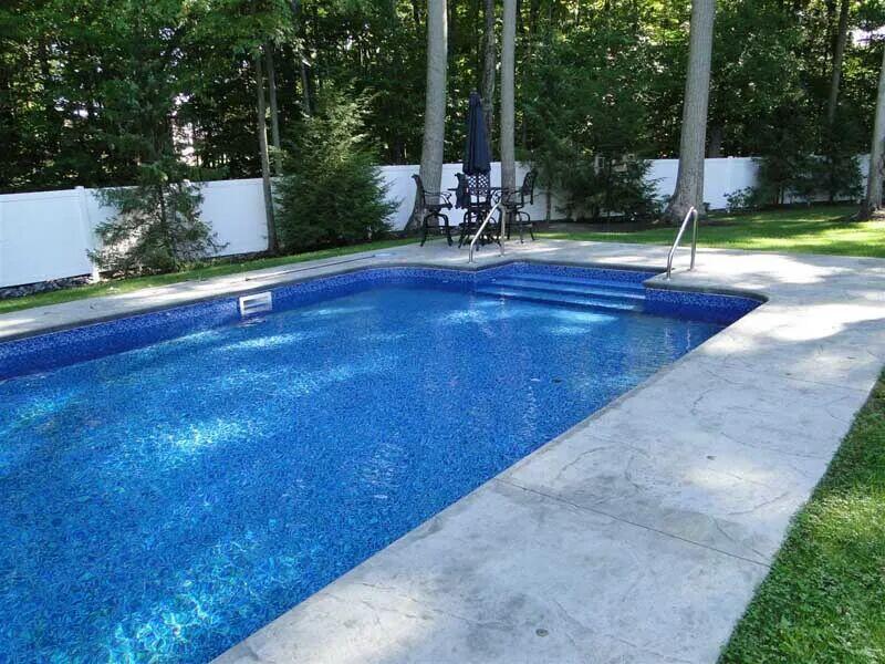 Inground pool with tan stamped concrete deck and white fence