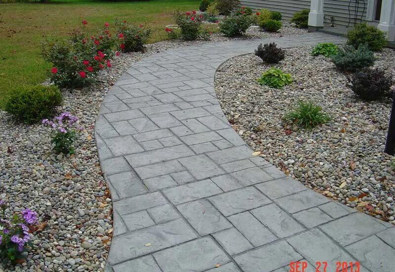 Curved ashlar stamped walkway with river rock beds and roses