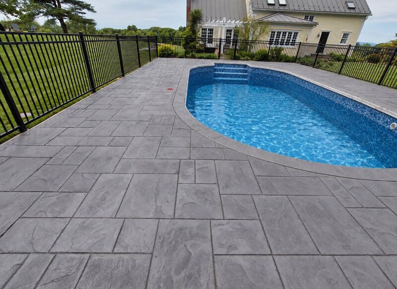 Gray ashlar stamped pool deck oval pool iron fence yellow farmhouse