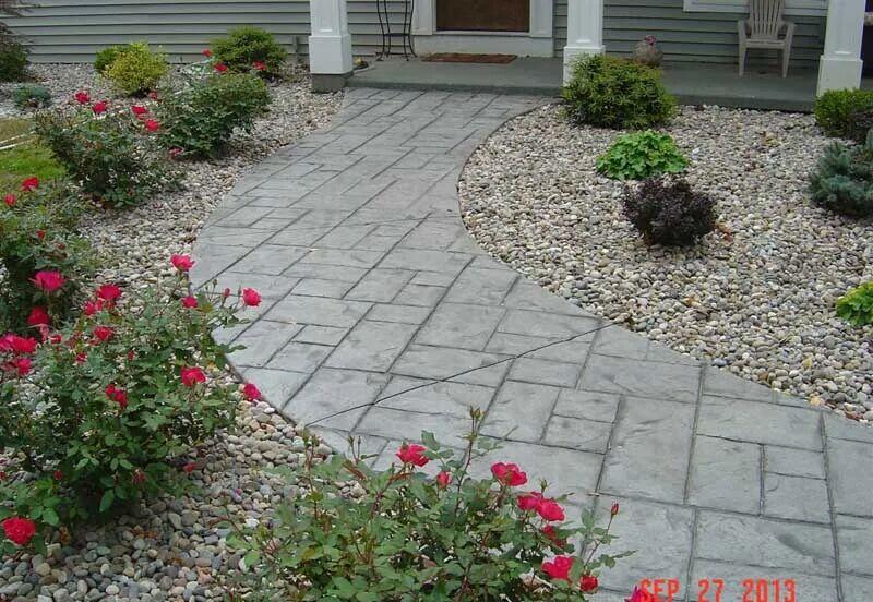Curved gray stamped ashlar walkway through river rock beds with roses