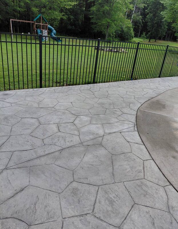 Gray random flagstone stamped pool deck iron fence treeline